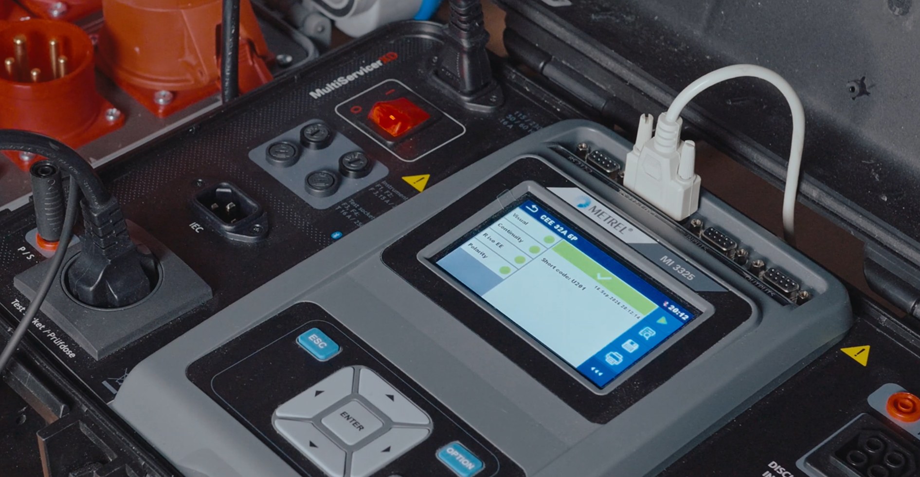 Metrel electrical test instrument in front of a connected test panel.