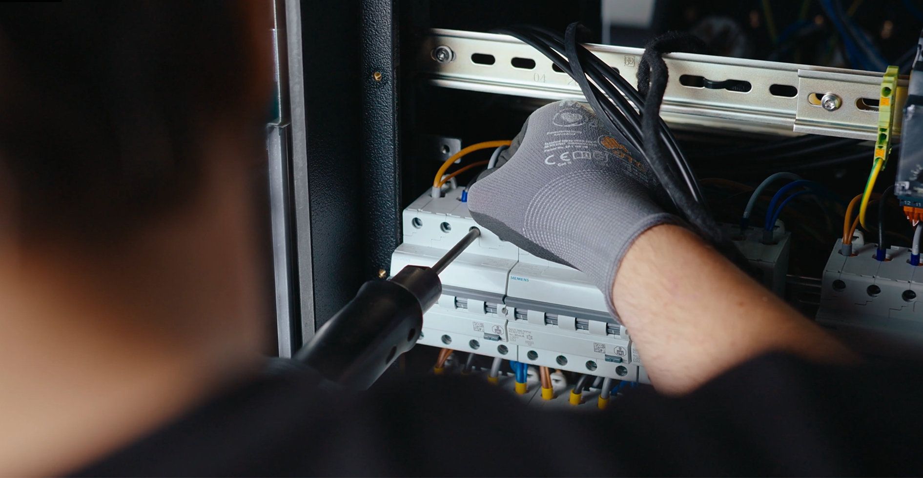 Gloved technician securing wiring to Siemens circuit breakers during PDU assembly.