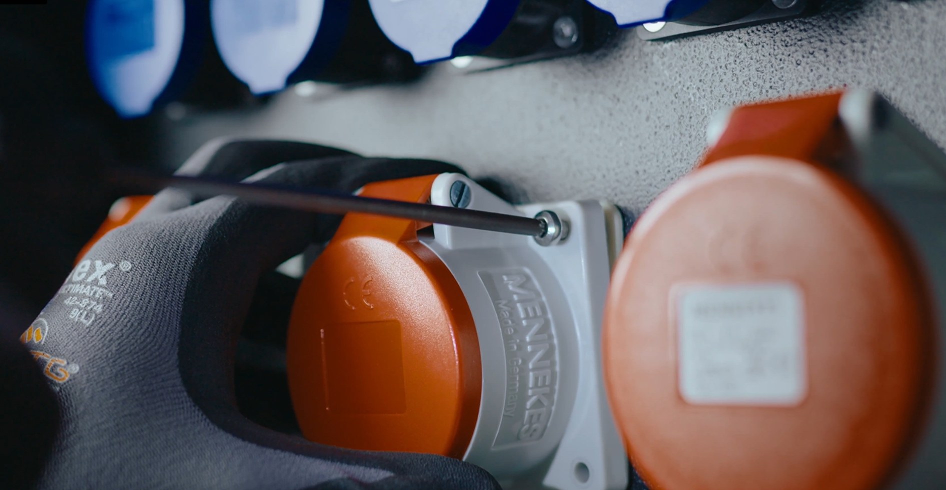 Close-up of a gloved technician tightening a red CEE panel socket fixing.
