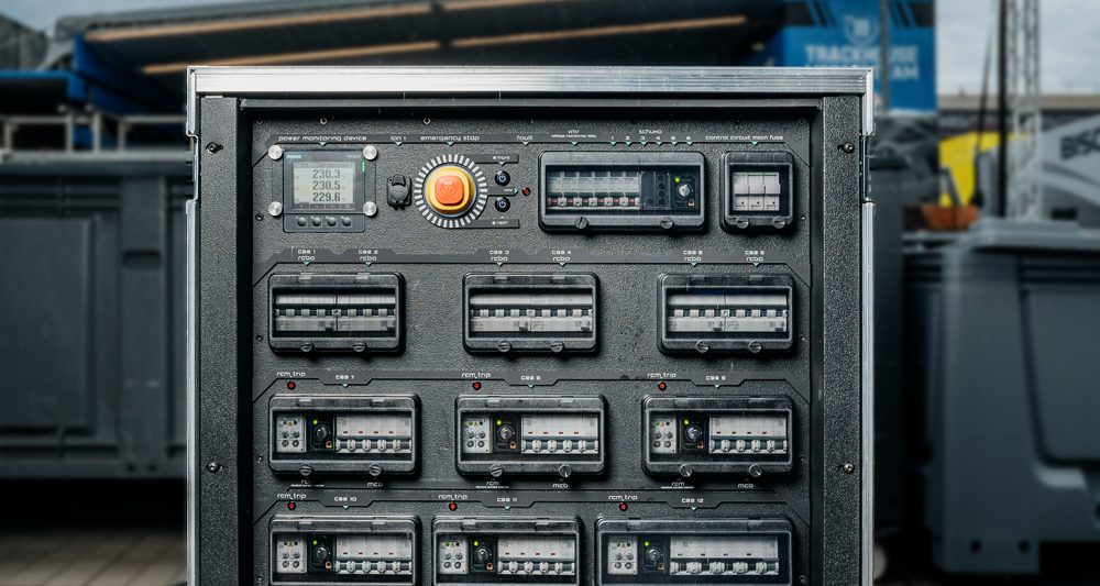 Flightcase PDU front panel with a power monitor, emergency stop and circuit breaker windows in a workshop.