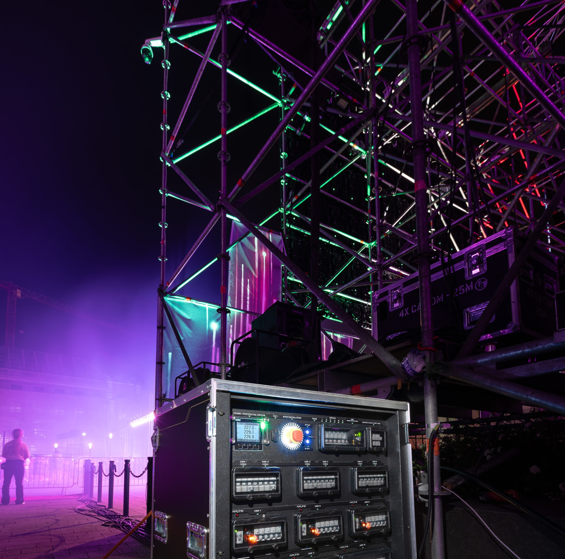 Power distribution unit beside a stage truss illuminated with green and purple lights.